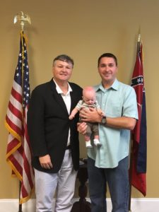 Brian Miller holds baby Noah next to staffer from Congressman's office. In the back are United States and state of Mississippi flags.