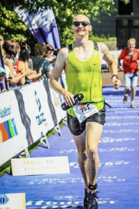 Markus runs in a race holding a water bottle to keep cool while bystanders cheer him on.