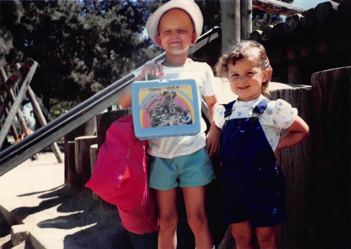 Sean Vora holds a lunchbox while his sister, Aubrey, wearing overalls stands next to him.