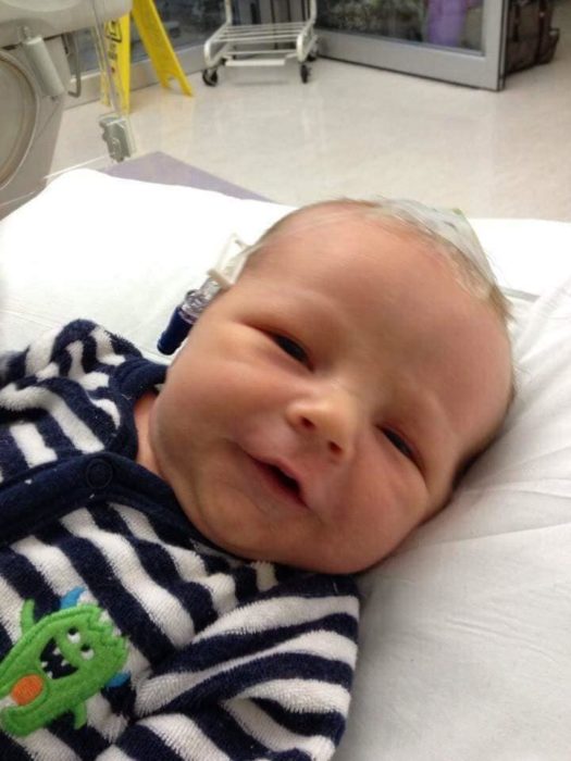 A baby boy wearing a blue and white striped sleeper lays on a baby bed. He has an IV in his scalp.