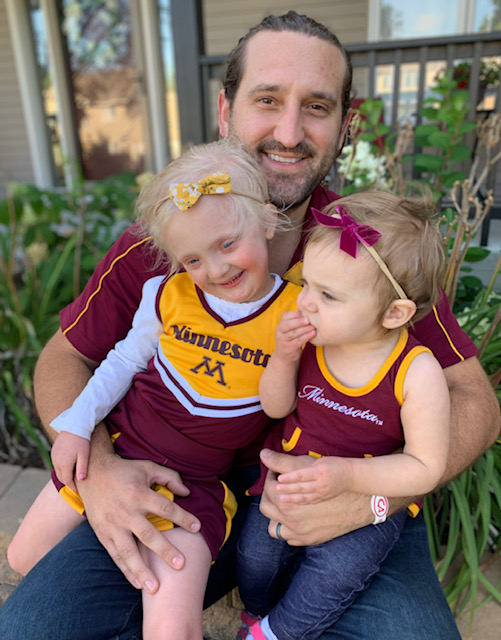 Tyler sits with his two daughters on his lap. The girls are wearing cheerleading uniforms.
