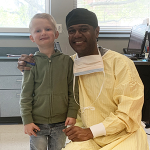 A boy is standing with his dentist, Dr. Simancas. The dentist is wearing scrubs.