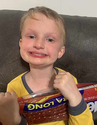 Four-year-old boy with XLHED smiles and holds a bag of strawberry licorice