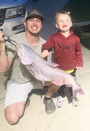A dad holds a very large fish that he caught. His son affected by hypohidrotic ectodermal dysplasia touches the fish.