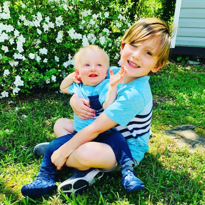 A boy in a blue shirt is holding his little brother who is affected by hypohidrotic ectodermal dysplasia.