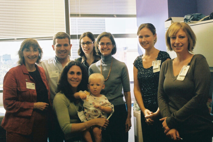 Six doctors stand in a hospital office with a mom and toddler who is affected by AEC syndrome. 
