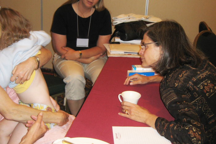 Dr. Siegfried is looking at the skin on the back of a child with ectodermal dysplasia. The mom holding the child has her shirt pulled up. Another woman in the background looks on.