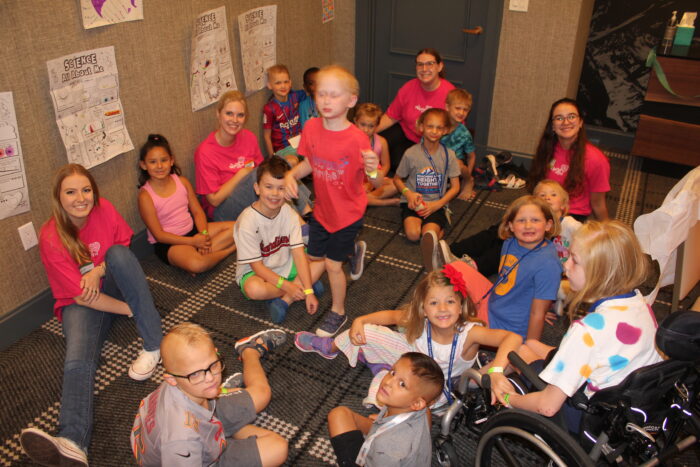 Children sit in a circle at Kids Camp getting ready to play a game.