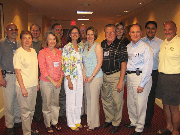 Eight men and five women post in a group shot in a conference hallway.
