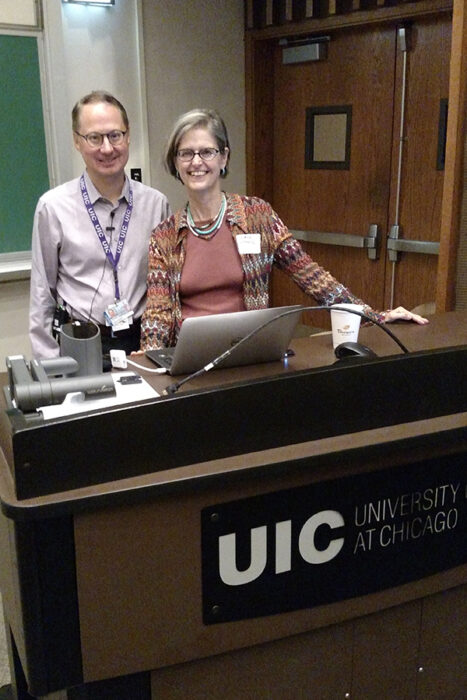Dr. Stanford and Dr. Siegfried are standing behind a podium with a laptop and microphone on it.