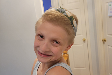 A girl with short blonde hair is wearing a head band and smiling.