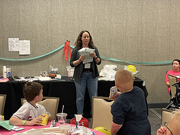 Dr. Marik stands in front of a group of children and is holding a bundle of papers.