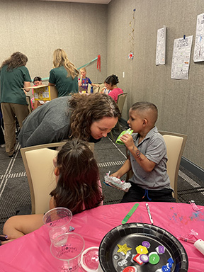 Dr. Marik is leaning down to listen to a child share something in her ear.