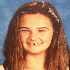 Lexie's grade school photo where she has a bow in her long blue hair and is smiling. She has a gap between her two front teeth.